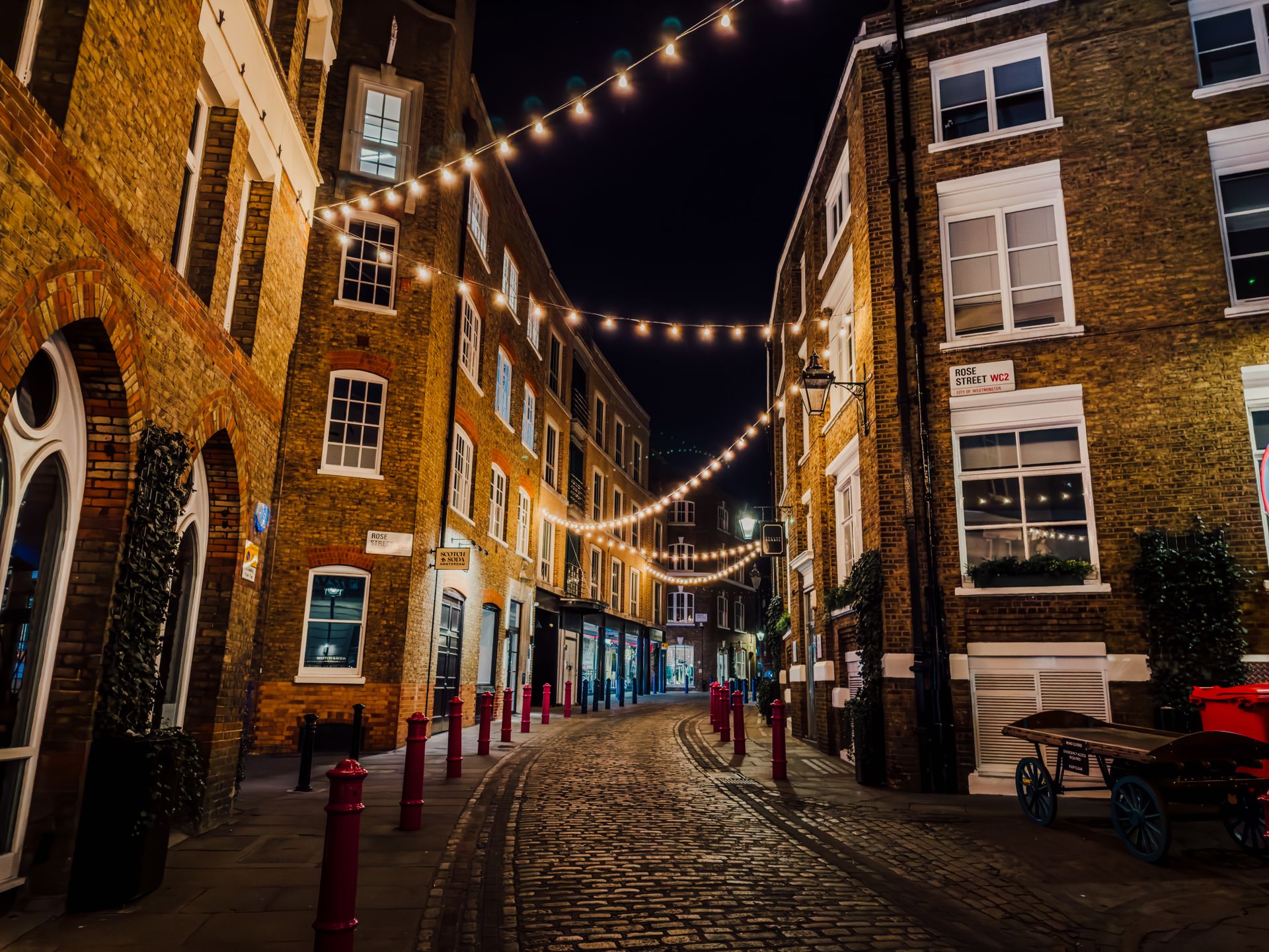 cobblestone street in Soho, London with string lights and historic buildings at night